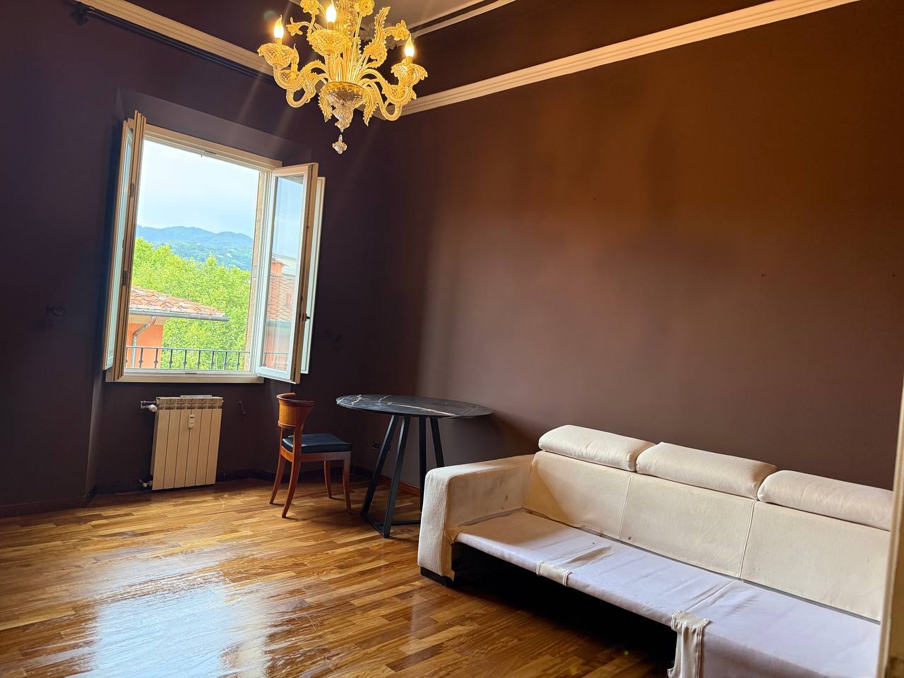 Soggiorno con pareti tinteggiate marrone cioccolato, cornici bianche al soffitto, lampadario di Murano e parquet